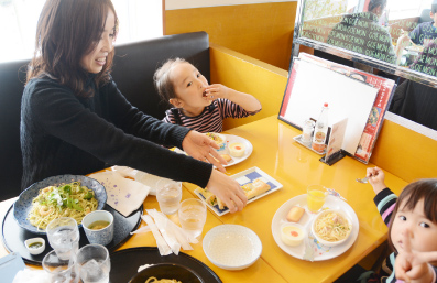 お母さんと小さな子供二人がレストランで食事している写真