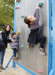 公園内の遊具で子供二人が遊んでいて、お母さんが見ている写真